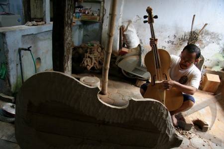 An Indonesian luthier working on a Keroncong Cello. Note there are only three pegs.